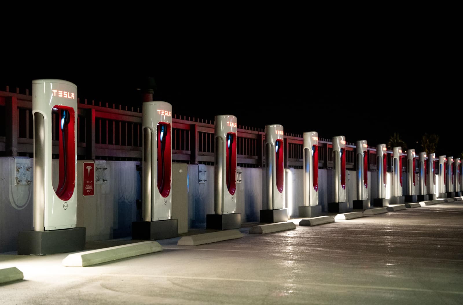 A row of Tesla Supercharger stations illuminated at night in a parking lot