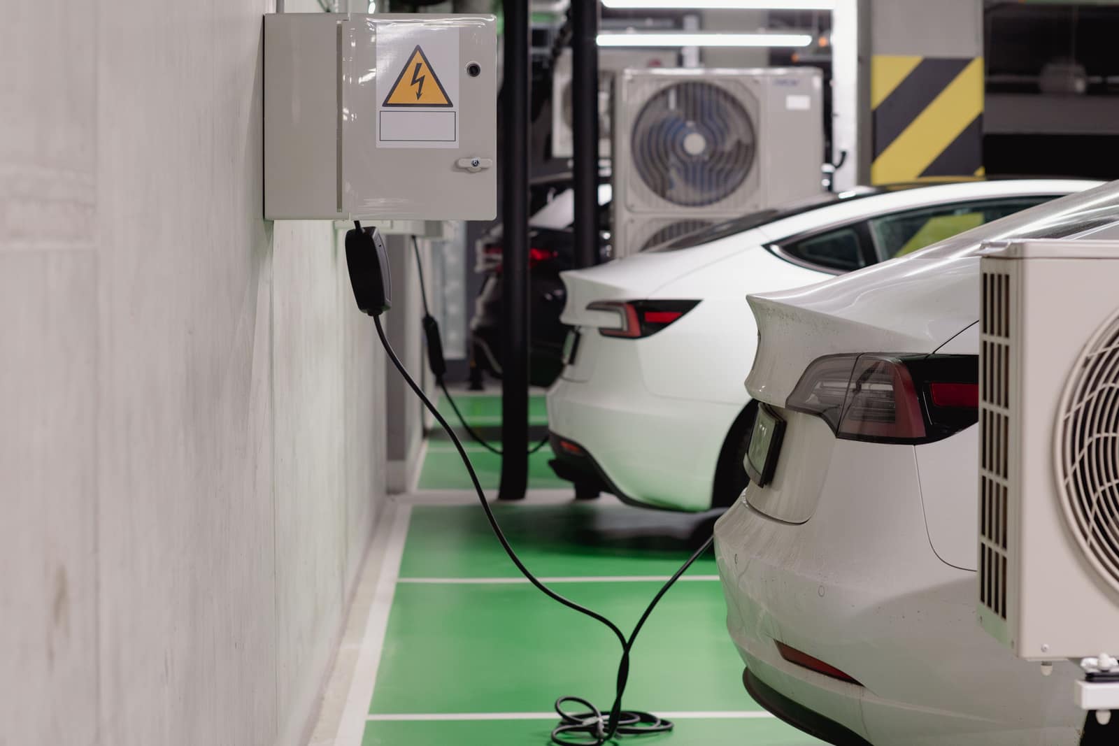 A charging cable running from a wall unit across marked bays in an underground parking garage
