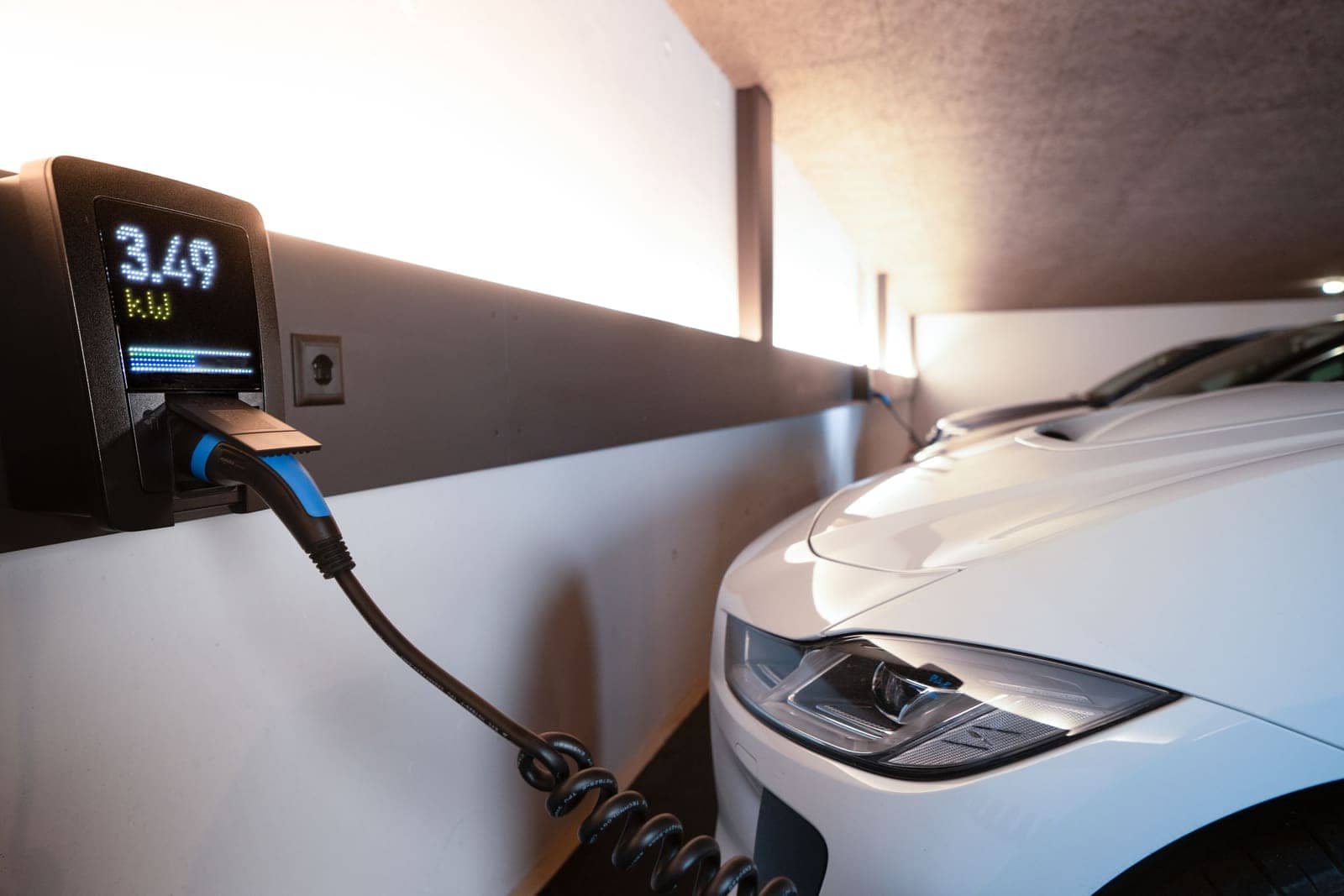 An electric car charging indoors from a wall-mounted charging unit