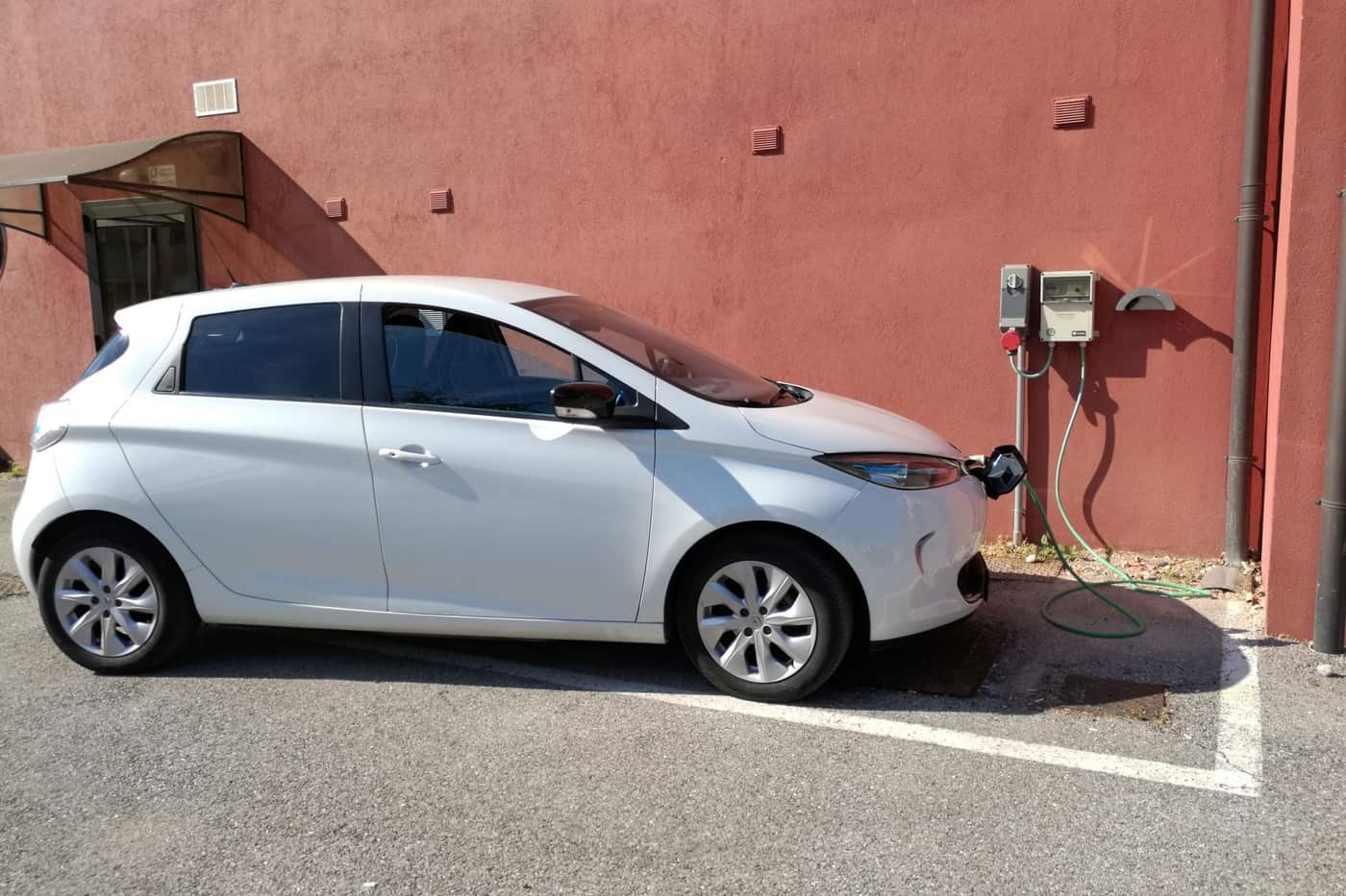 An electric car charging from a plain wall-mounted socket in an ordinary parking bay
