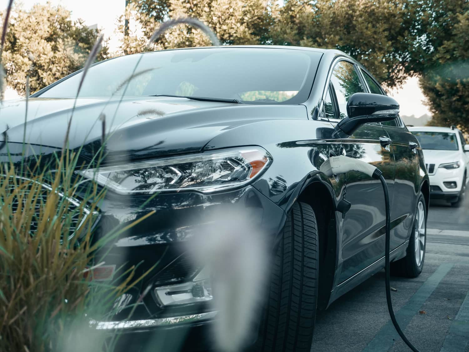 A dark plug-in hybrid sedan charging from a cable at an outdoor parking space
